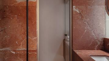 A modern bathroom with a marble floor, a glass shower enclosure, and a sink with a mirror.