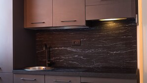 Une cuisine moderne avec des meubles de couleur sombre, un dosseret en marbre et un évier en acier inoxydable.