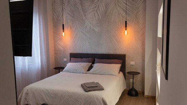A bedroom with a bed, two bedside tables, a nightstand, and a wall with a leaf pattern.