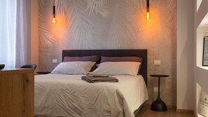 A bedroom with a bed, two wall-mounted light fixtures, a bedside table, and a small round table.