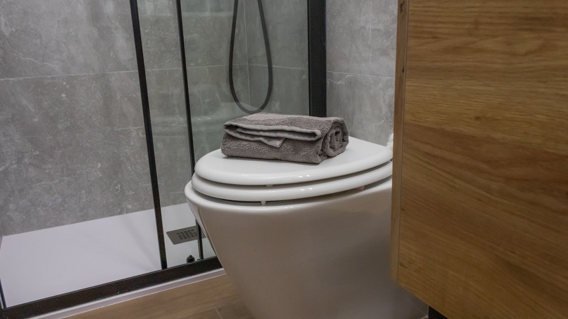 Ein Badezimmer mit Toilette, Duschkabine aus Glas und einem hölzernen Waschtisch.