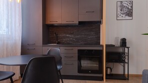 A modern kitchen with dark countertops, a built-in oven, and a dining area with a table and chairs.