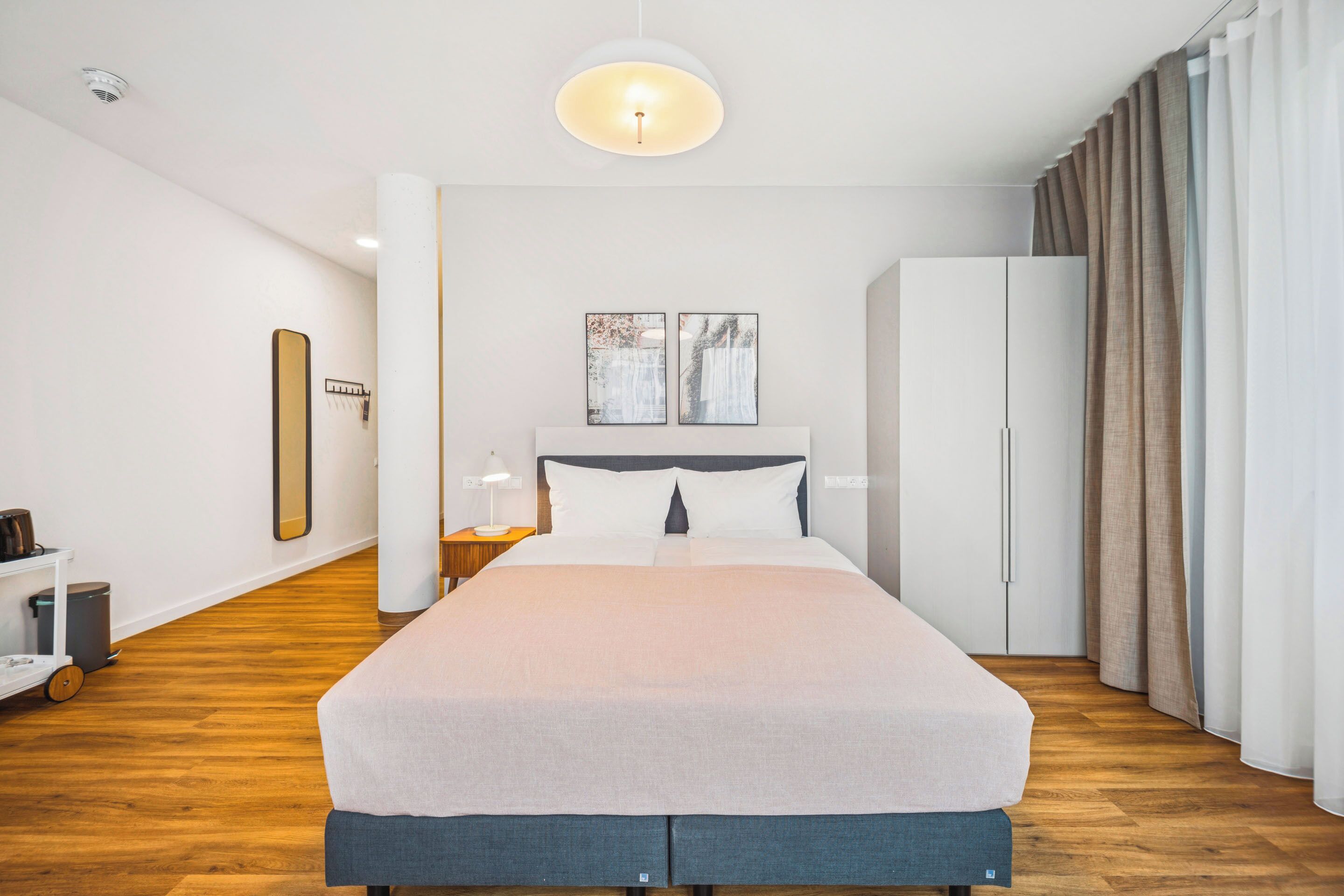 A modern hotel room with a large bed, a wardrobe, a nightstand, and a ceiling light.