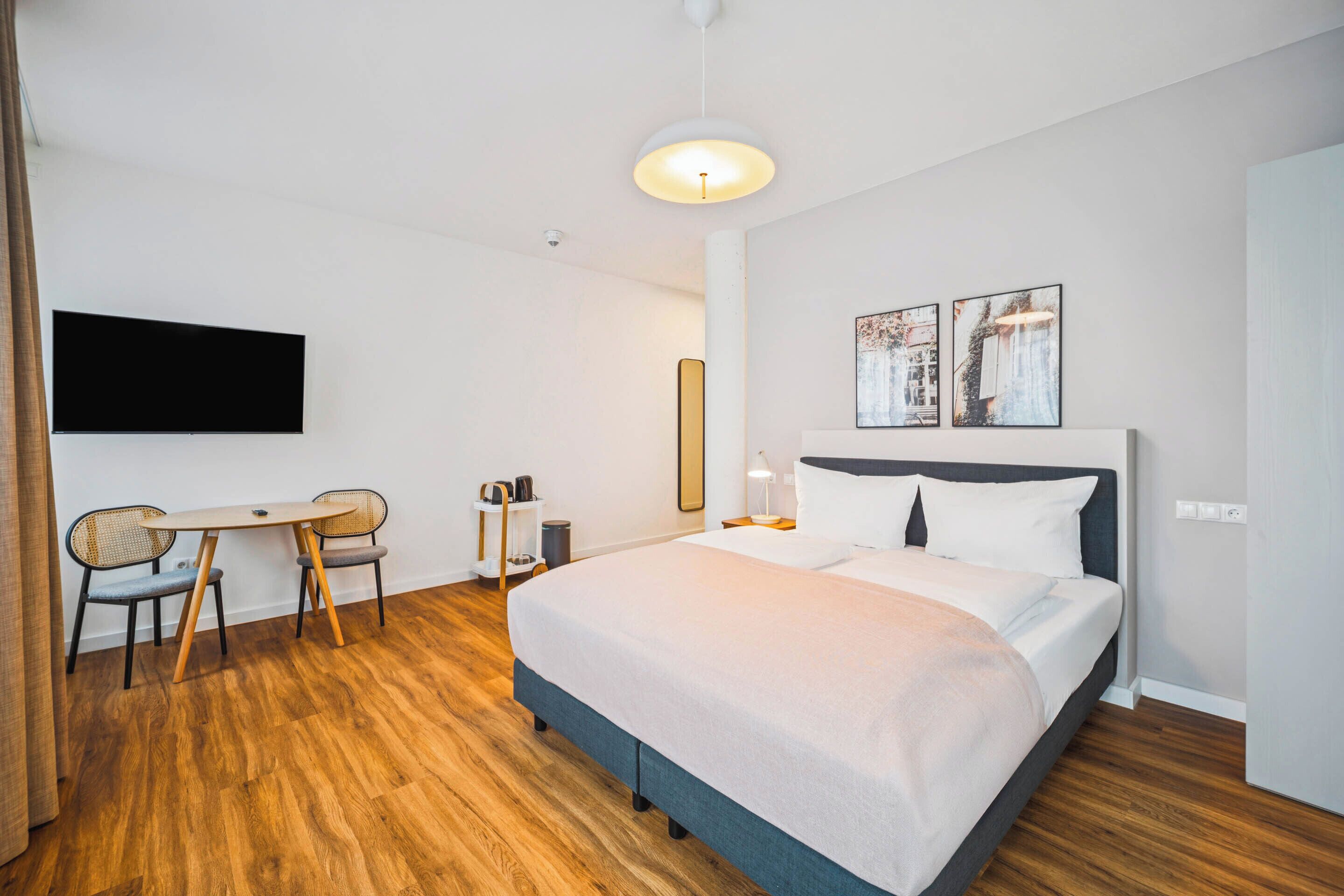 Habitación de hotel moderna con una cama grande, un escritorio con sillas, un televisor de pantalla plana y dos cuadros en la pared.
