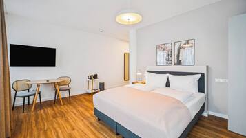 Habitación de hotel moderna con una cama grande, un escritorio con sillas, un televisor de pantalla plana y dos cuadros en la pared.