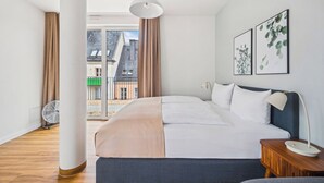Un dormitorio moderno con una cama grande, una mesita de noche con lámpara y dos cuadros en la pared.