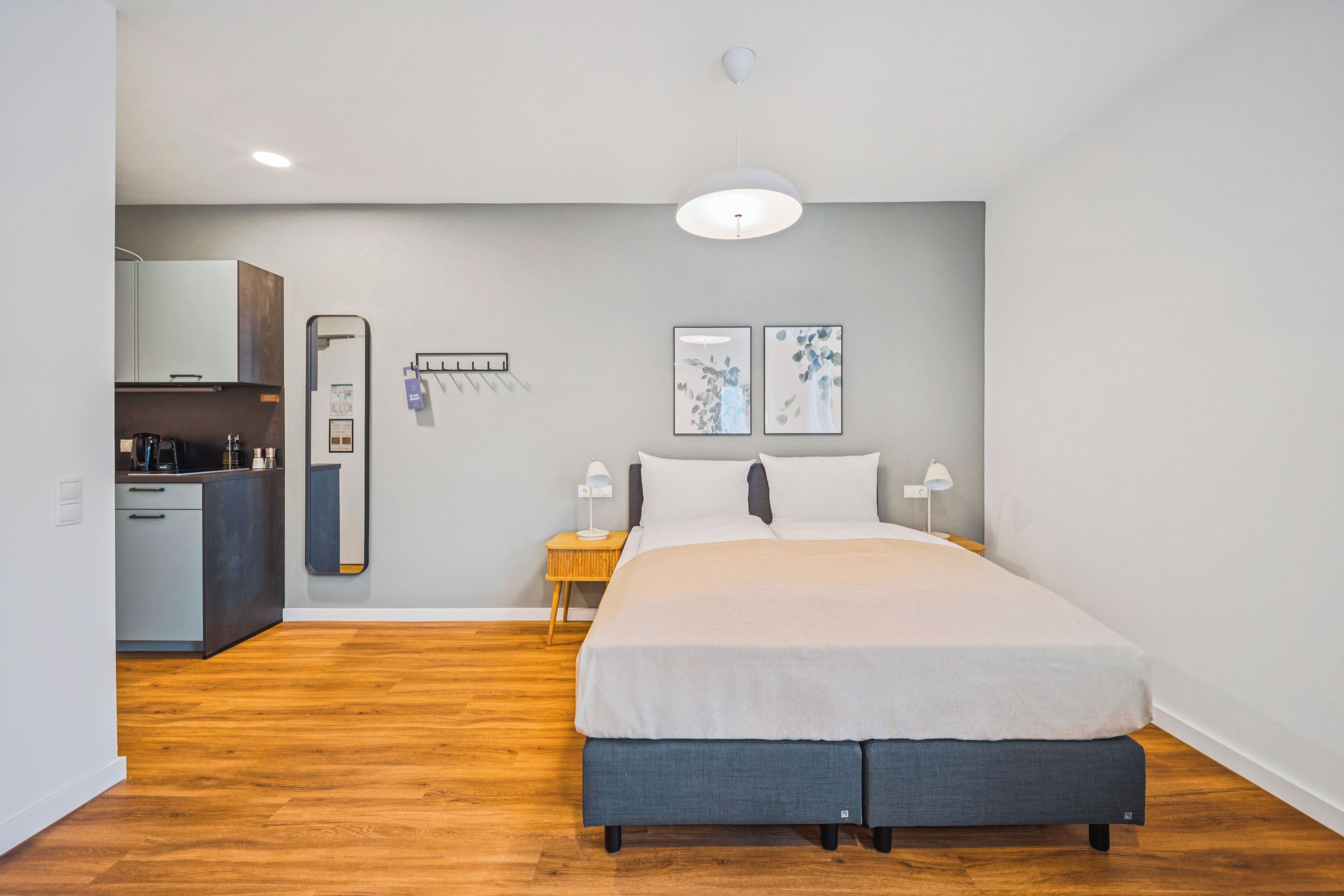 Une chambre moderne comprenant un lit, des tables de chevet, un miroir et une petite kitchenette.