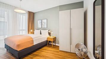 Une chambre moderne avec un grand lit, une table de chevet avec une lampe, un ventilateur sur pied et une armoire.