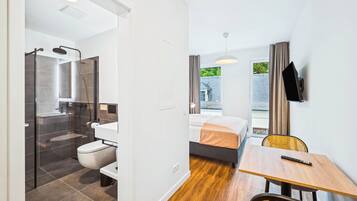A modern hotel room with a shower, toilet, bed, and a dining area with a table and chairs.