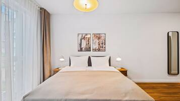 A neatly made bed with a neutral-toned bedspread, two bedside lamps, and a large mirror on the wall.
