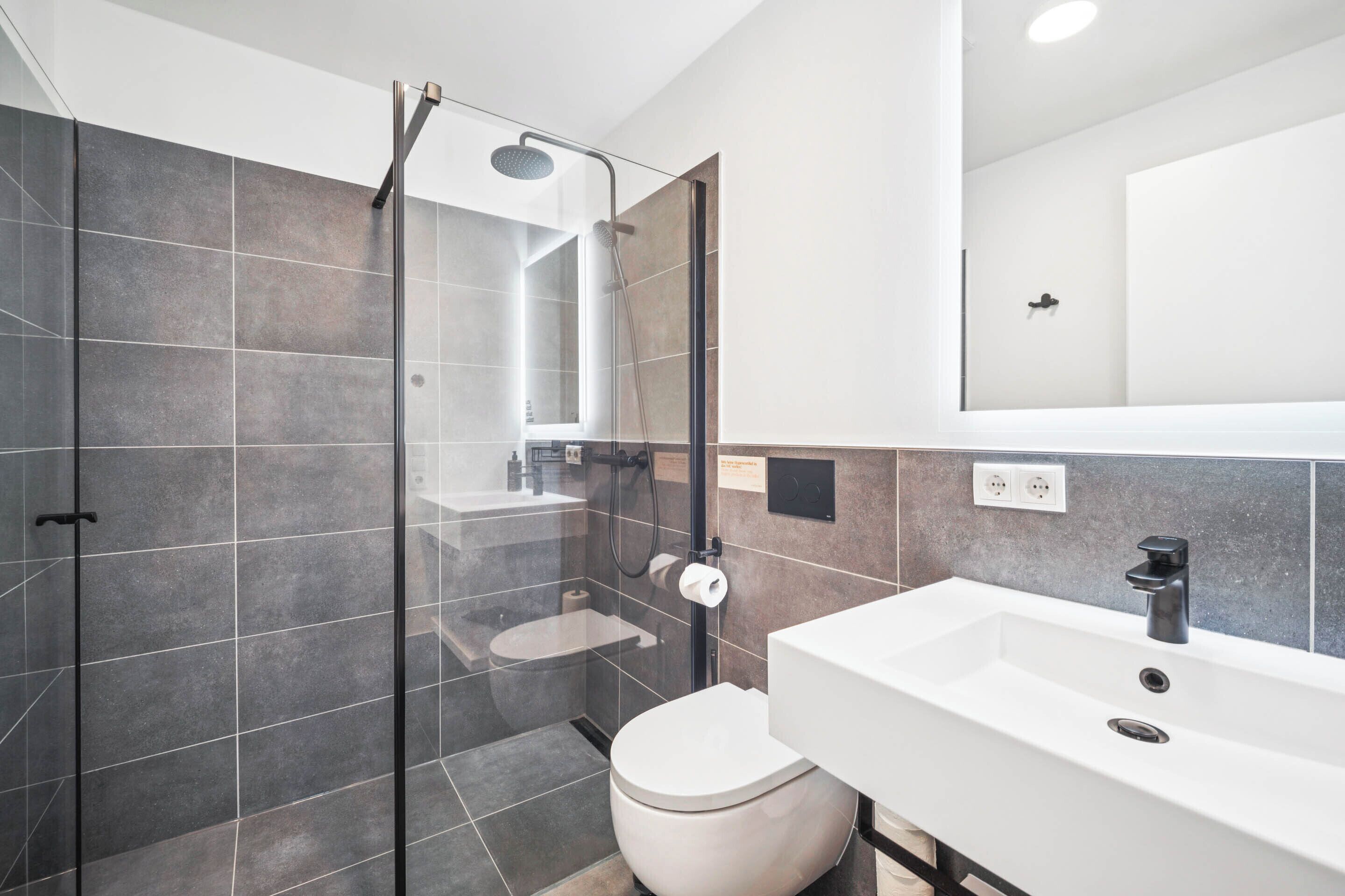 A modern bathroom with a glass-enclosed shower, a white sink, and a toilet.