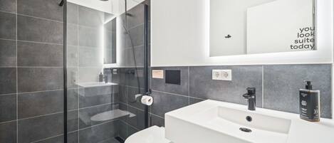 A modern bathroom with a glass-enclosed shower, a white sink, and a toilet.