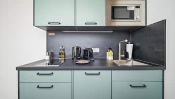 A compact kitchen with teal cabinets, a stainless steel microwave, a coffee maker, and a sink.