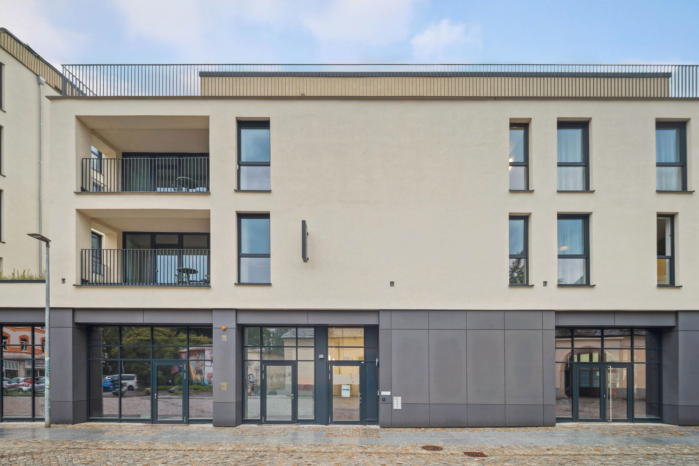 A modern building with a flat facade, large windows, and a gated entrance.