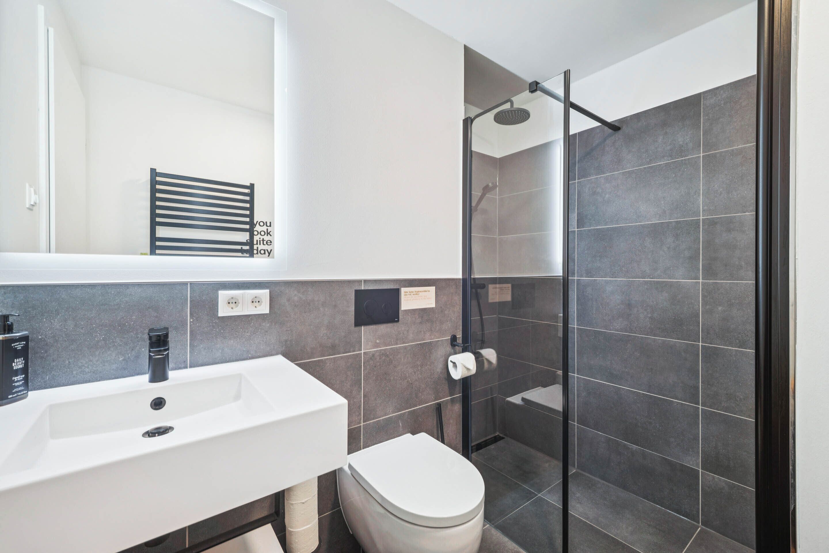 Un bagno moderno con lavandino bianco, rubinetto nero e doccia con porta in vetro.