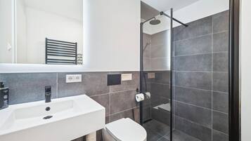 Un bagno moderno con lavandino bianco, rubinetto nero e doccia con porta in vetro.