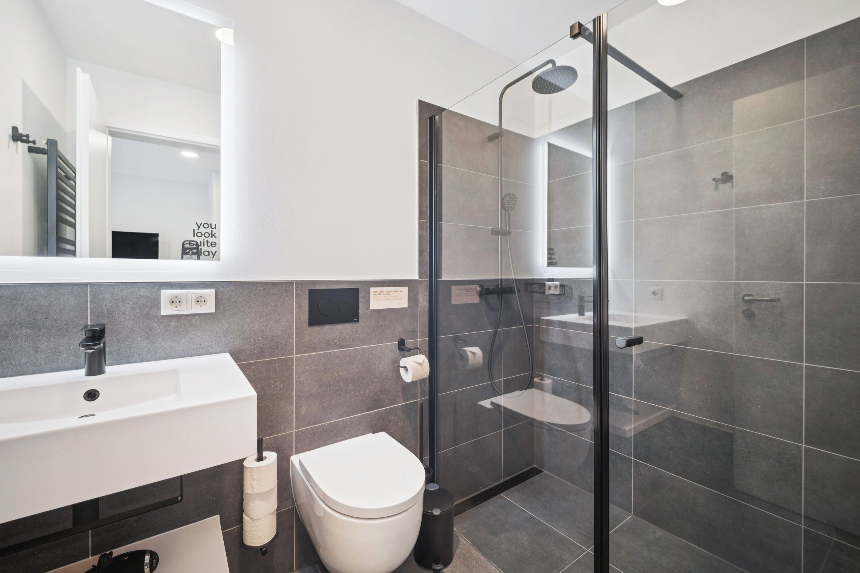 A modern bathroom with a glass-enclosed shower, a white sink, and a toilet.