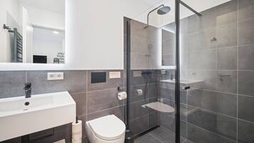 A modern bathroom with a glass-enclosed shower, a white sink, and a toilet.