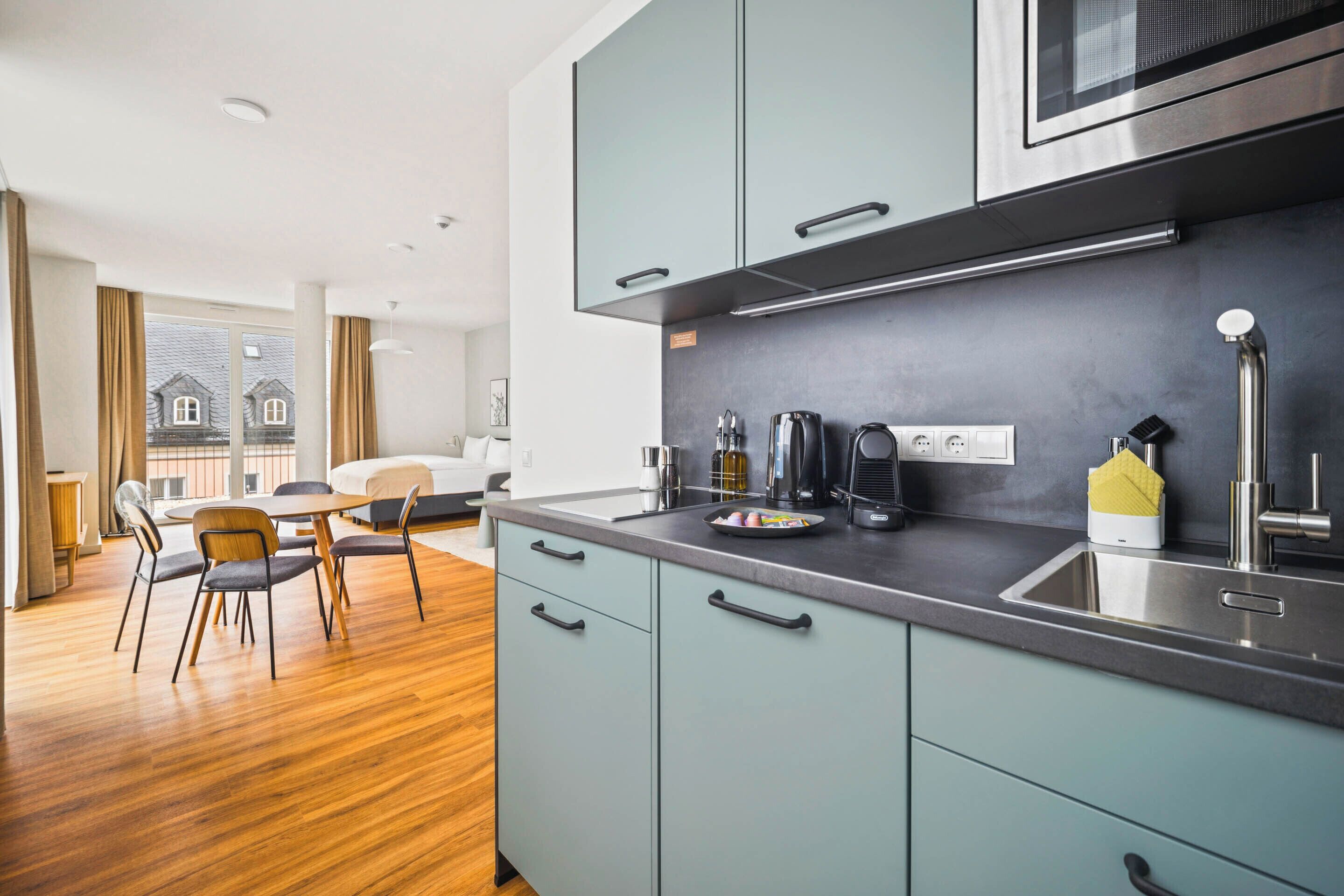 Une cuisine moderne avec des meubles gris, des appareils en acier inoxydable et un coin repas doté d’un plancher et de chaises en bois.