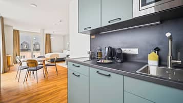A modern kitchen with grey cabinets, stainless steel appliances, and a dining area with wooden flooring and chairs.