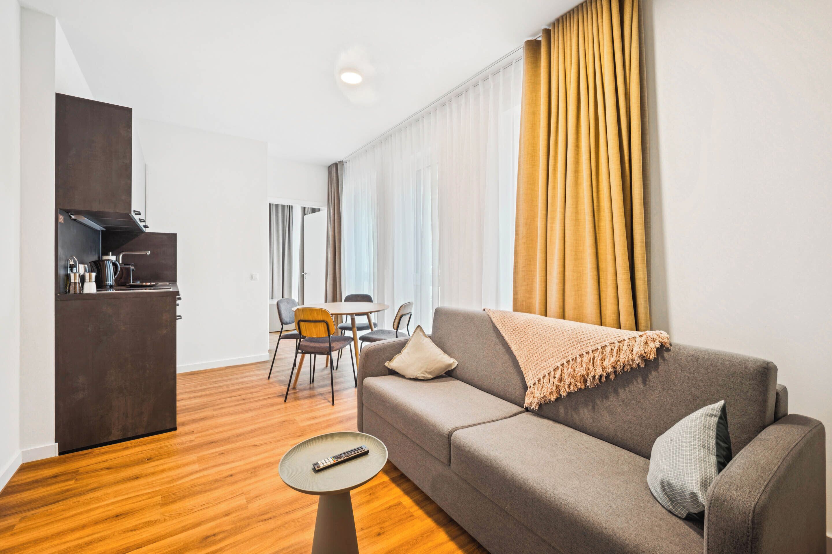 Una sala de estar moderna con un sofá, una mesita redonda y una zona de cocina con estufa empotrada.