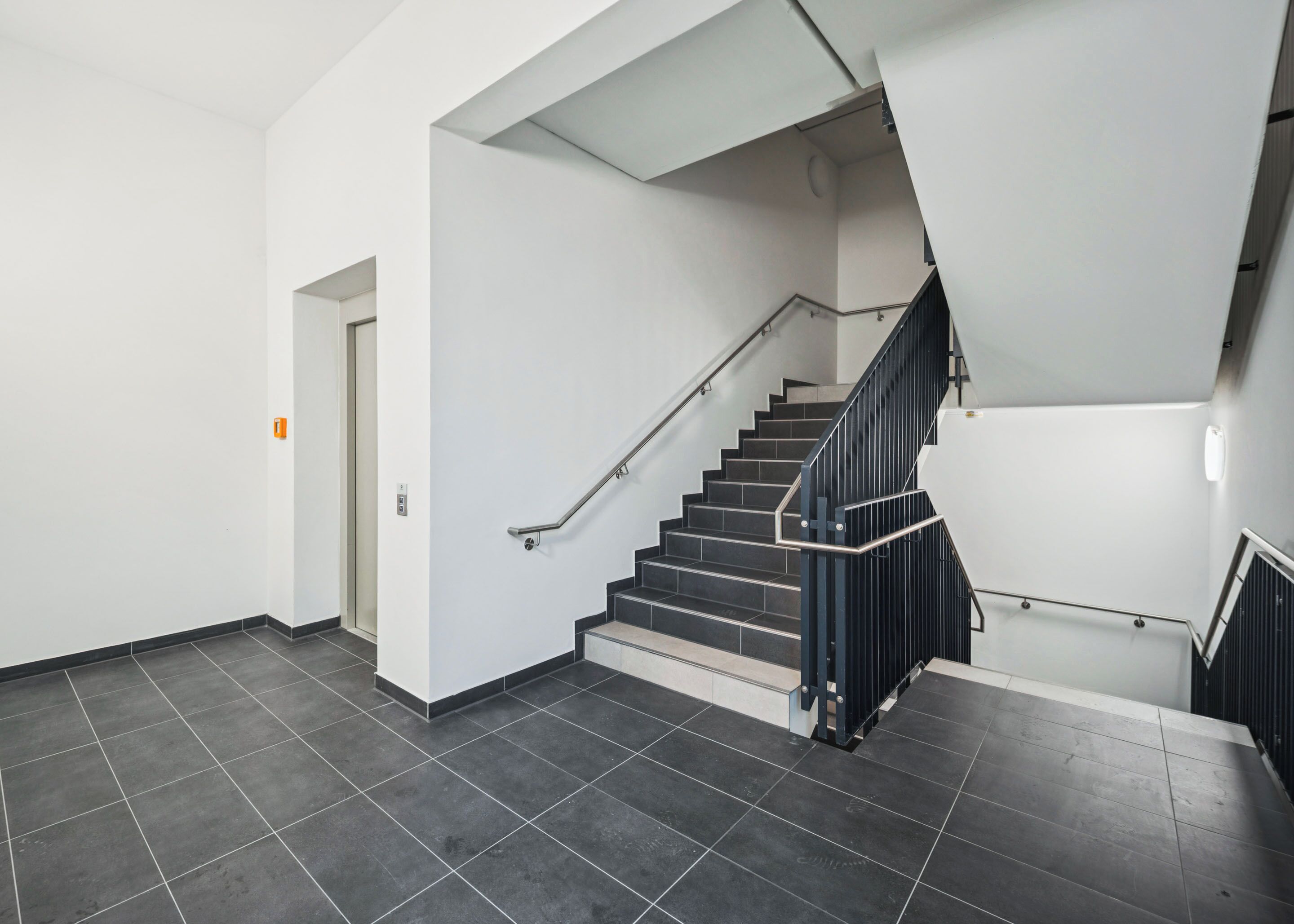 Una escalera moderna con barandillas negras y pasamanos, que conduce a un rellano con una pared blanca y una puerta.