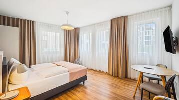 Ein modernes Hotelzimmer mit Bett, Schreibtisch, Stuhl, Ventilator und Fernseher.