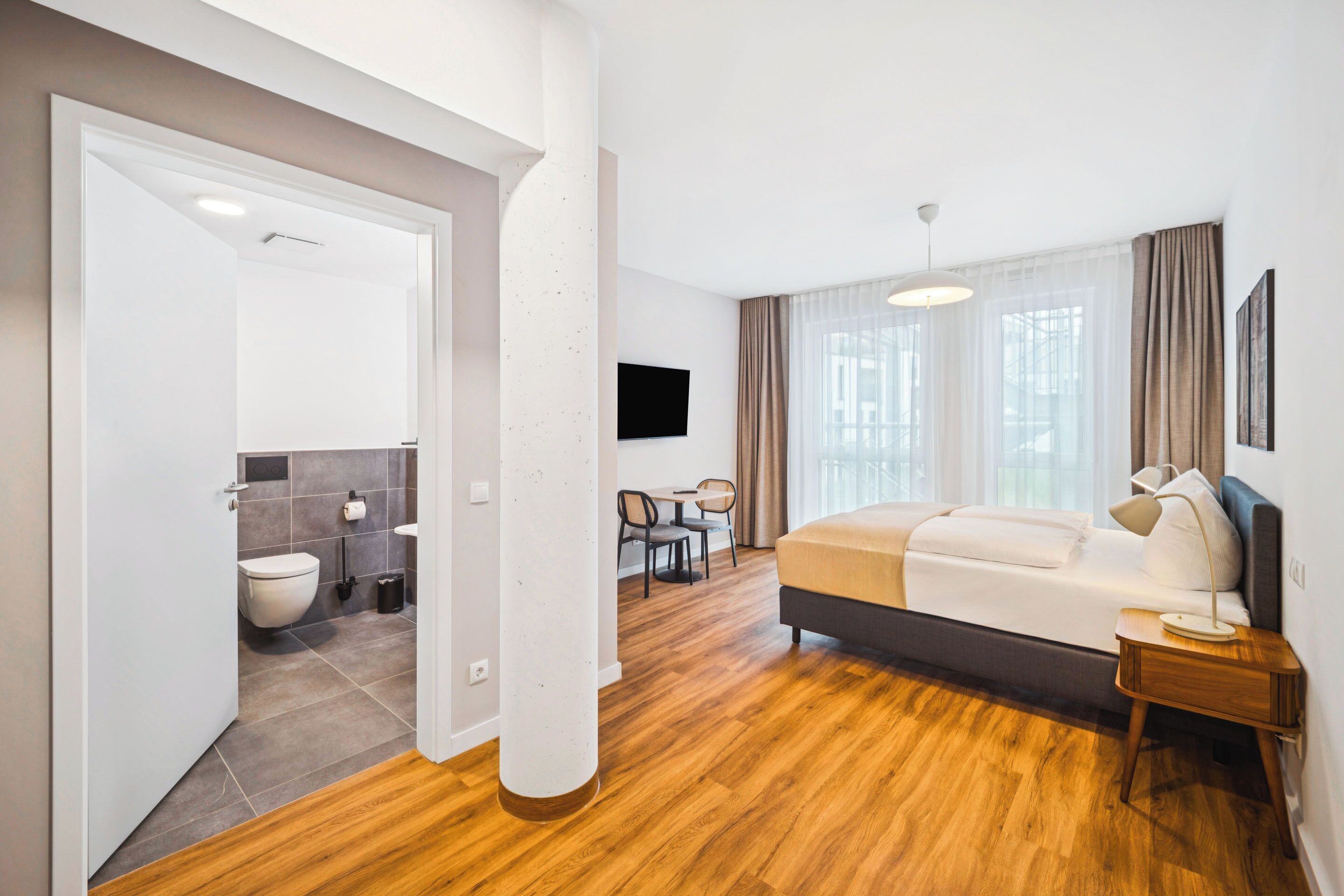 Una habitación de hotel moderna con piso de madera, una cama, un escritorio y un televisor.