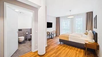 Una habitación de hotel moderna con piso de madera, una cama, un escritorio y un televisor.