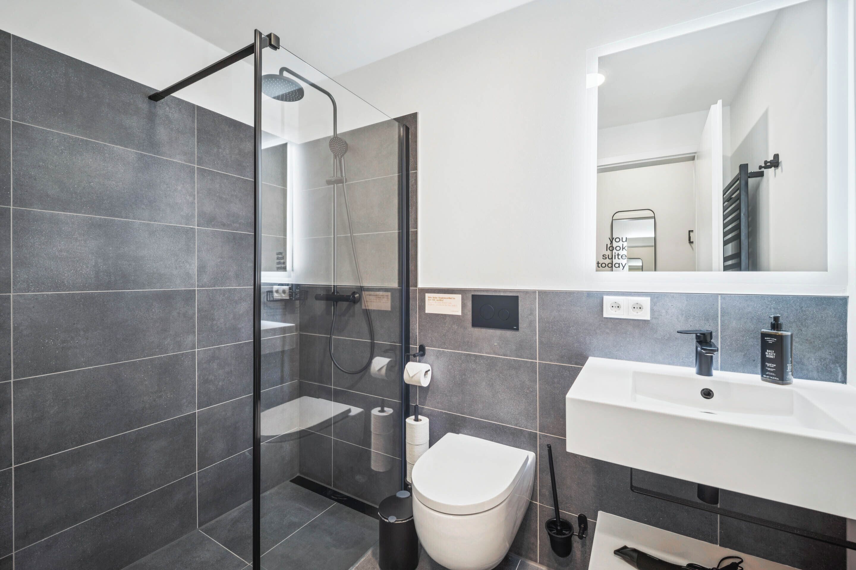 A modern bathroom with a glass-enclosed shower, a white sink, and a toilet.