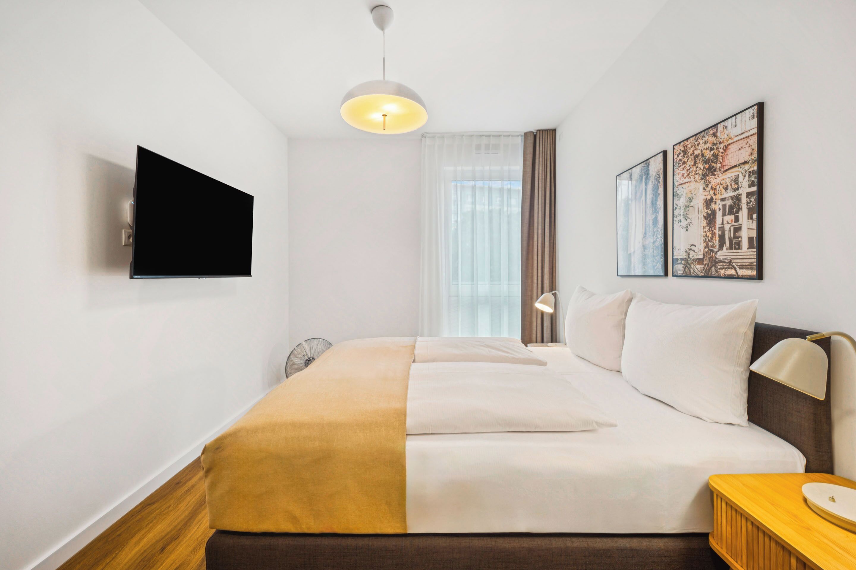 Ett hotellrum med en säng, en tv, en sänglampa och ett fönster med gardiner.