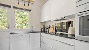 Une cuisine moderne avec des meubles blancs, un lave-vaisselle Bosch, une machine à café et un bloc à couteaux.