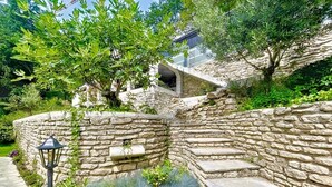 Un escalier en pierre menant à un bâtiment, entouré d’une végétation luxuriante et d’un mur de pierre.