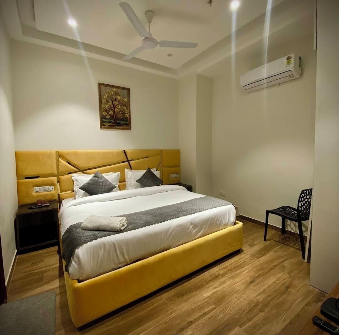 Une chambre avec un lit jaune, un ventilateur de plafond, un climatiseur et un tableau accroché au mur.