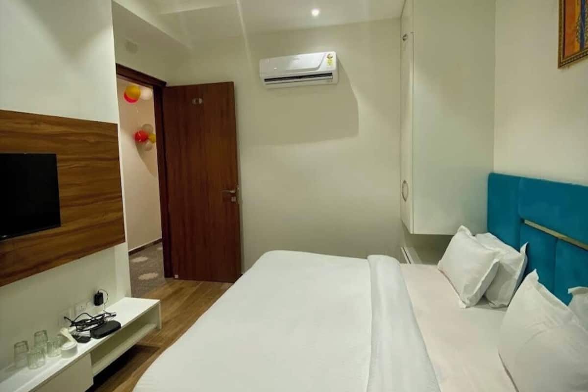A hotel room with a bed, a TV, an air conditioner, and a ceiling fan.