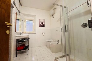 A bathroom with a glass shower enclosure, a white sink, a toilet, and a bidet. - Cozy apartment in historic center (Manziana)
