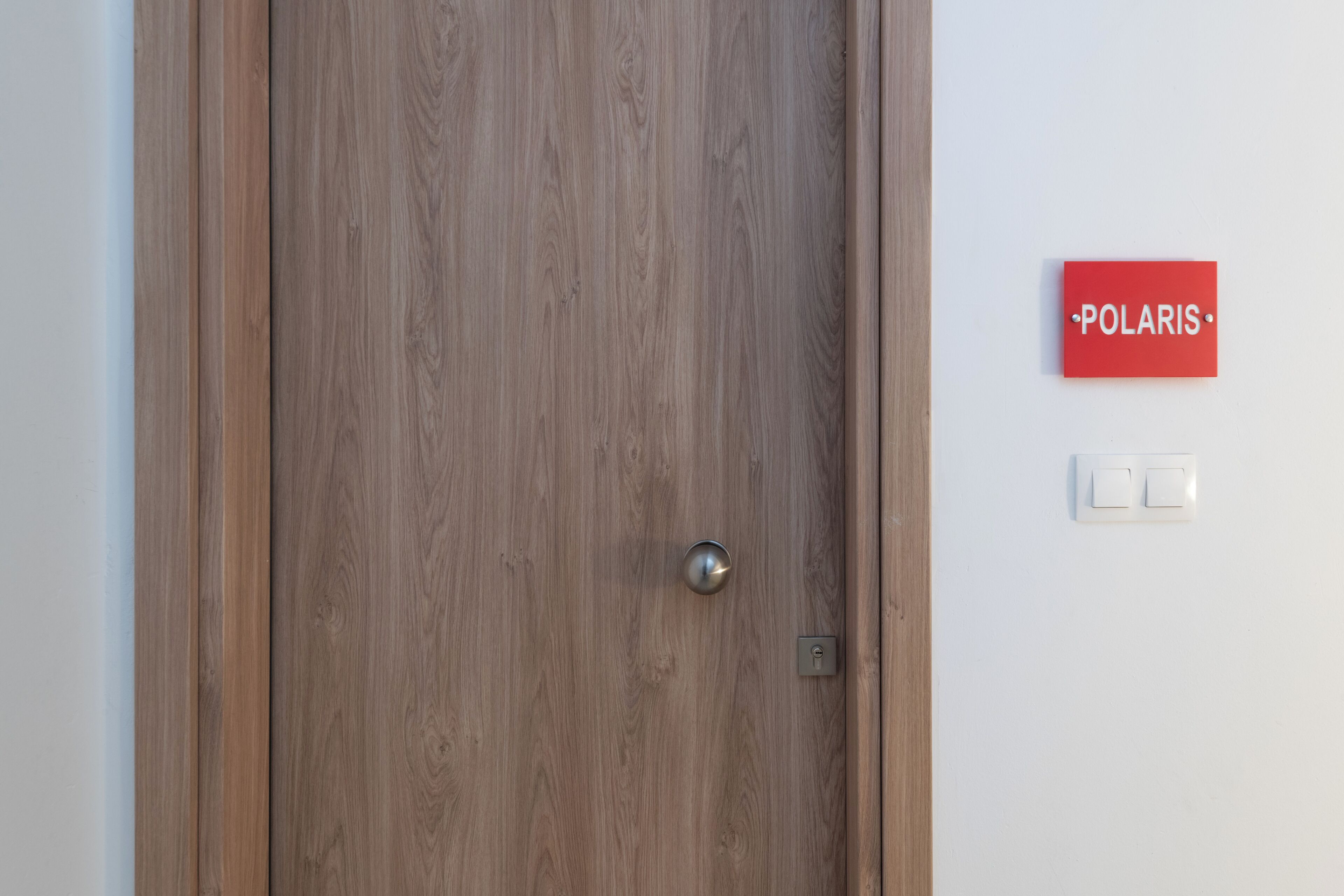 A wooden door with a metallic handle and a keyhole, a red sign with "POLARIS" text, and a light switch on the wall.