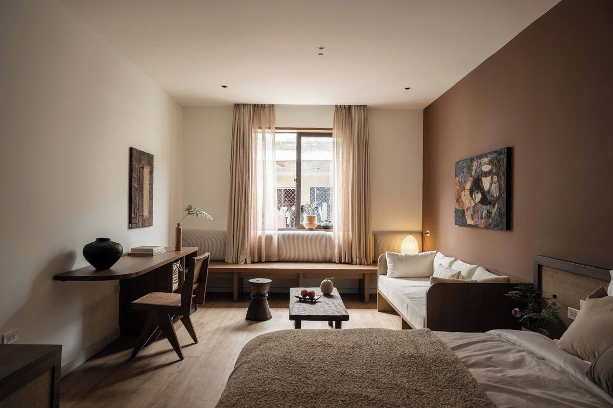 A hotel room with a bed, a desk, a chair, a small table, and a window with curtains.