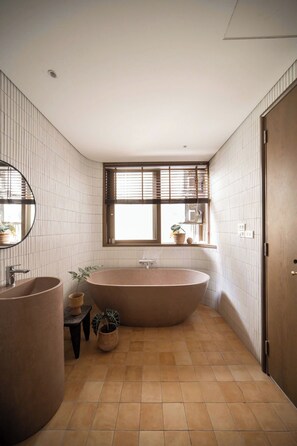A bathroom with a freestanding bathtub, a round sink, and a window with blinds. - A Stay In Hanoi (Hanoi)
