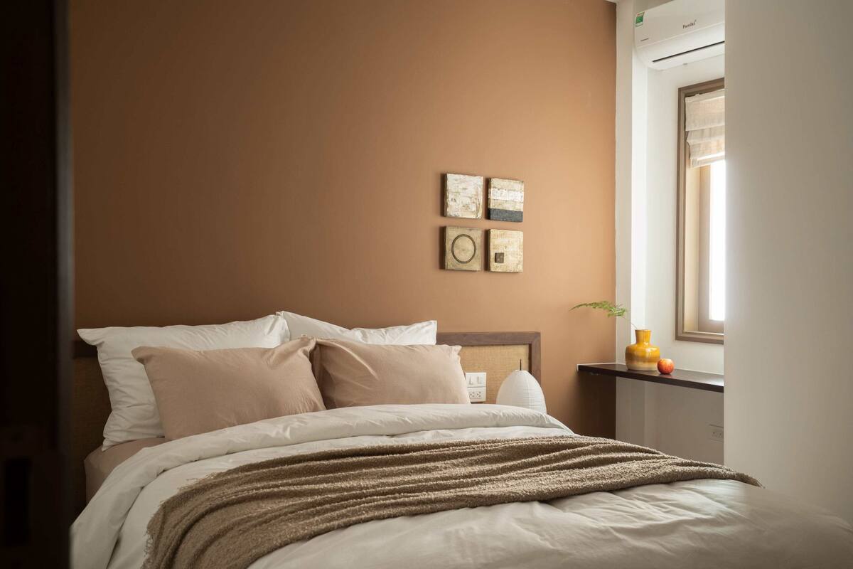 A bedroom with a bed, pillows, a blanket, a nightstand, a lamp, and wall art.