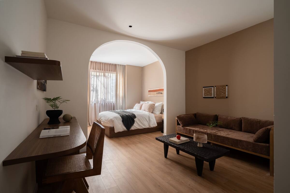 A modern, well-lit room with a bed, a sofa, a dining table, and a coffee table.
