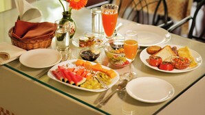 Una mesa de desayuno con diversos platos, un jarrón con flores y vistas al exterior con vegetación.