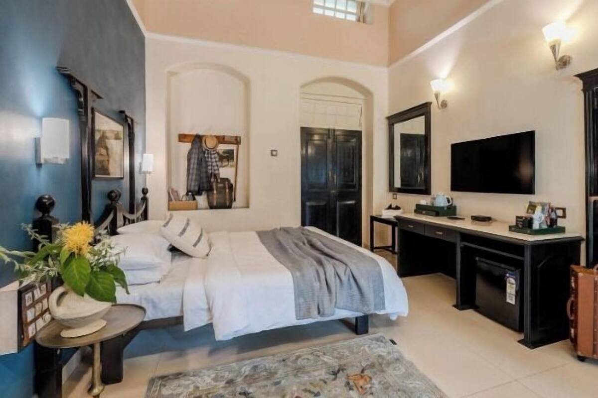 A bedroom with a bed, desk, TV, and a suitcase.
