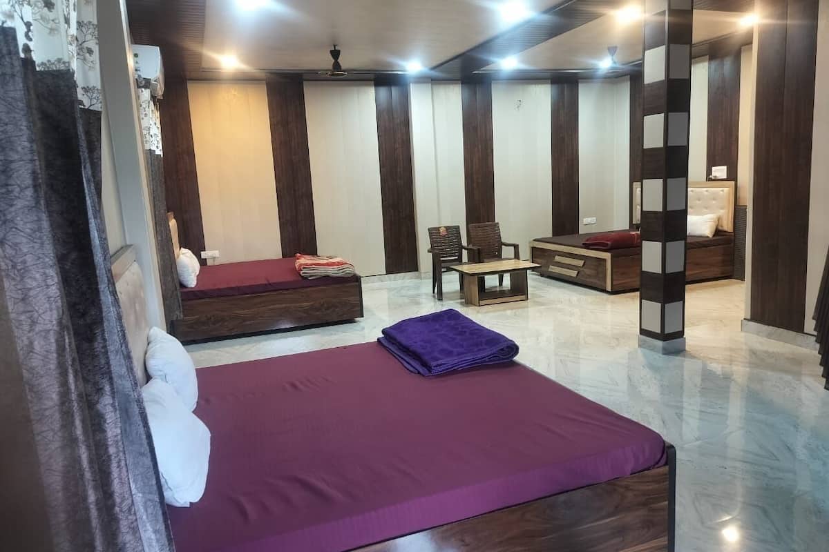 A hotel room with a large bed, a sofa, a small table, and a chair. There are curtains on the windows and a ceiling fan.