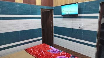 A small room with a bed, a television mounted on the wall, and a door.