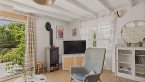 A living room with a television, a chair, a table with glasses, and a bookshelf. - Large garden and terrace – 4 adults and 1 child (Fouesnant)