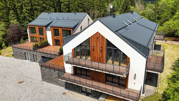 A modern two-story house with a sloped roof, large windows, and a balcony with wooden railings. - Rezidence Jezerní  (Železná Ruda)