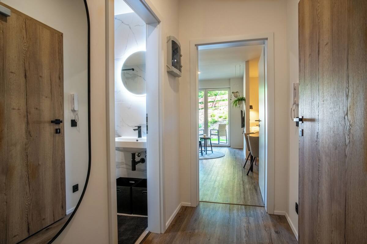 A hallway with wooden doors, a modern bathroom, and a view into a dining area with natural light.
