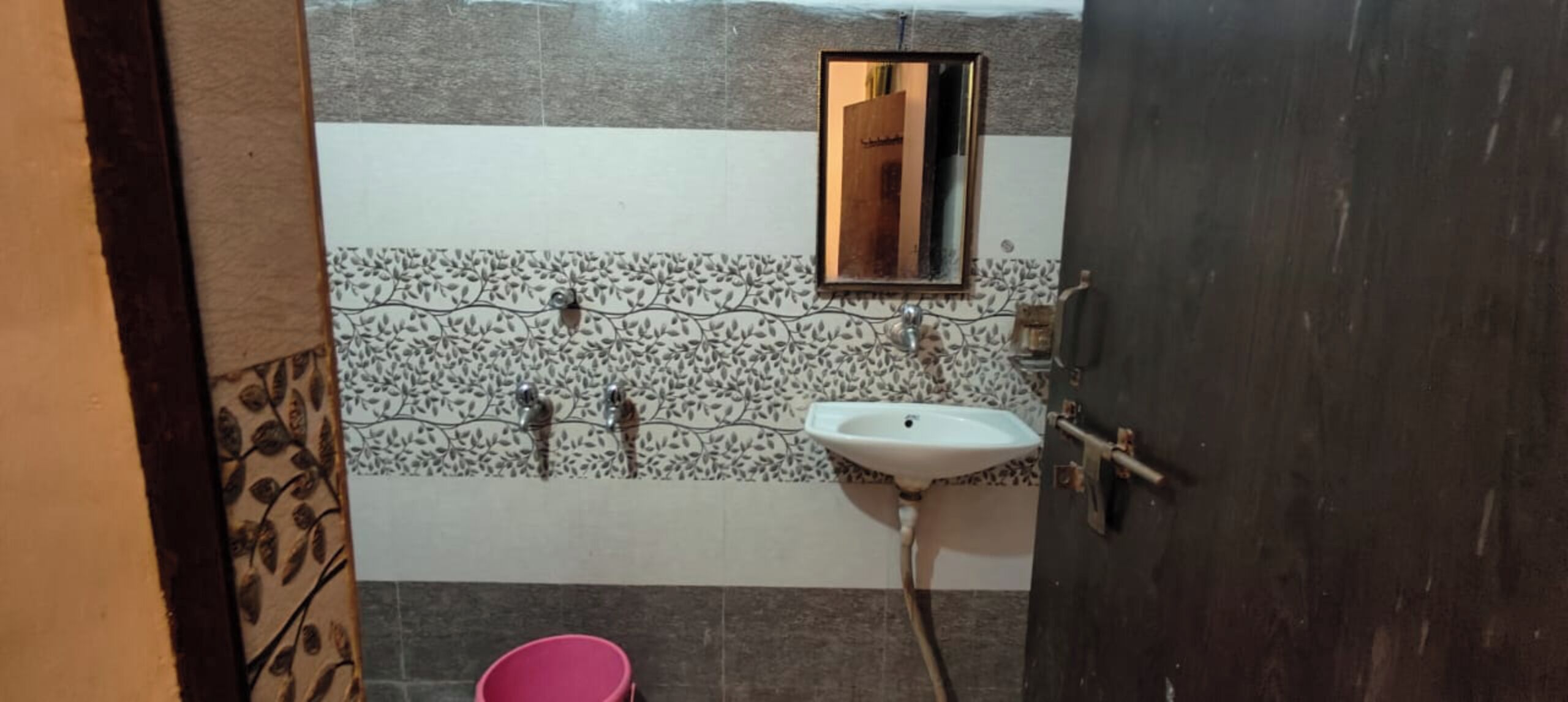 A bathroom with a white sink, two faucets, a mirror, and a pink bucket.