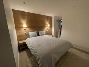 Quarto com cabeceira de madeira, duas luminárias de apoio, uma cama grande e um tapete estampado.
